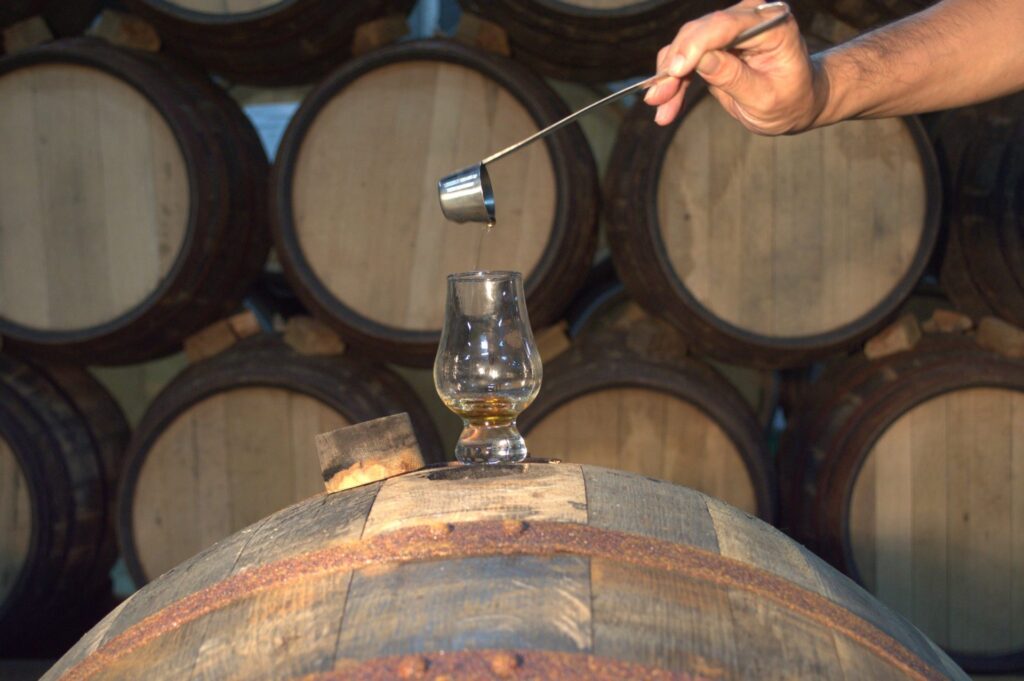 熟成庫で樽の上にグラスを置き、スポイトで原酒を垂らしたテイスティングの様子